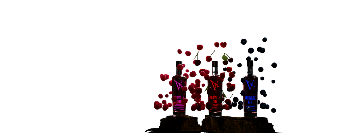 Piles of raspberries, cherries and blueberries around three Vaudville gin bottles